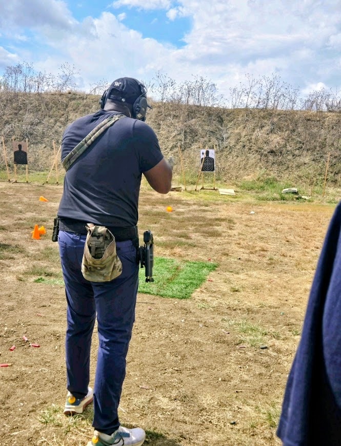 Gideon Training Solutions student at an outdoor shooting range engaging paper targets with a handgun during a live-fire defensive training session in DFW. Student wears hearing protection and a tactical holster rig while practicing marksmanship fundamentals and defensive shooting drills.